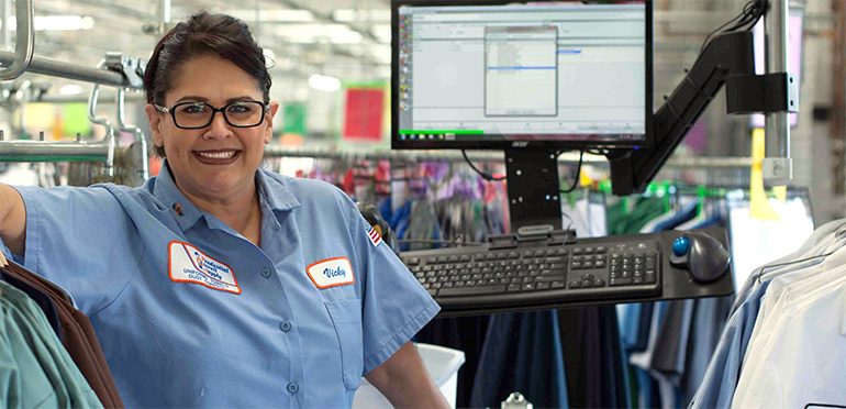 Smiling Woman With Blue Work Shirt On Standing In Front Of Computer