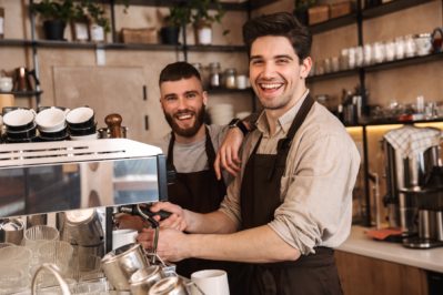 Group of cheerful men baristas wearing aprons