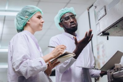 Woman working with African worker in food factory to checking and report machine problem to engineer in production line.