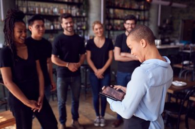 Female restaurant manager with tablet giving team talk to waiting staff