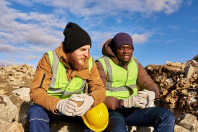 two industrial workers wearing reflective jackets, relaxing taking break from work