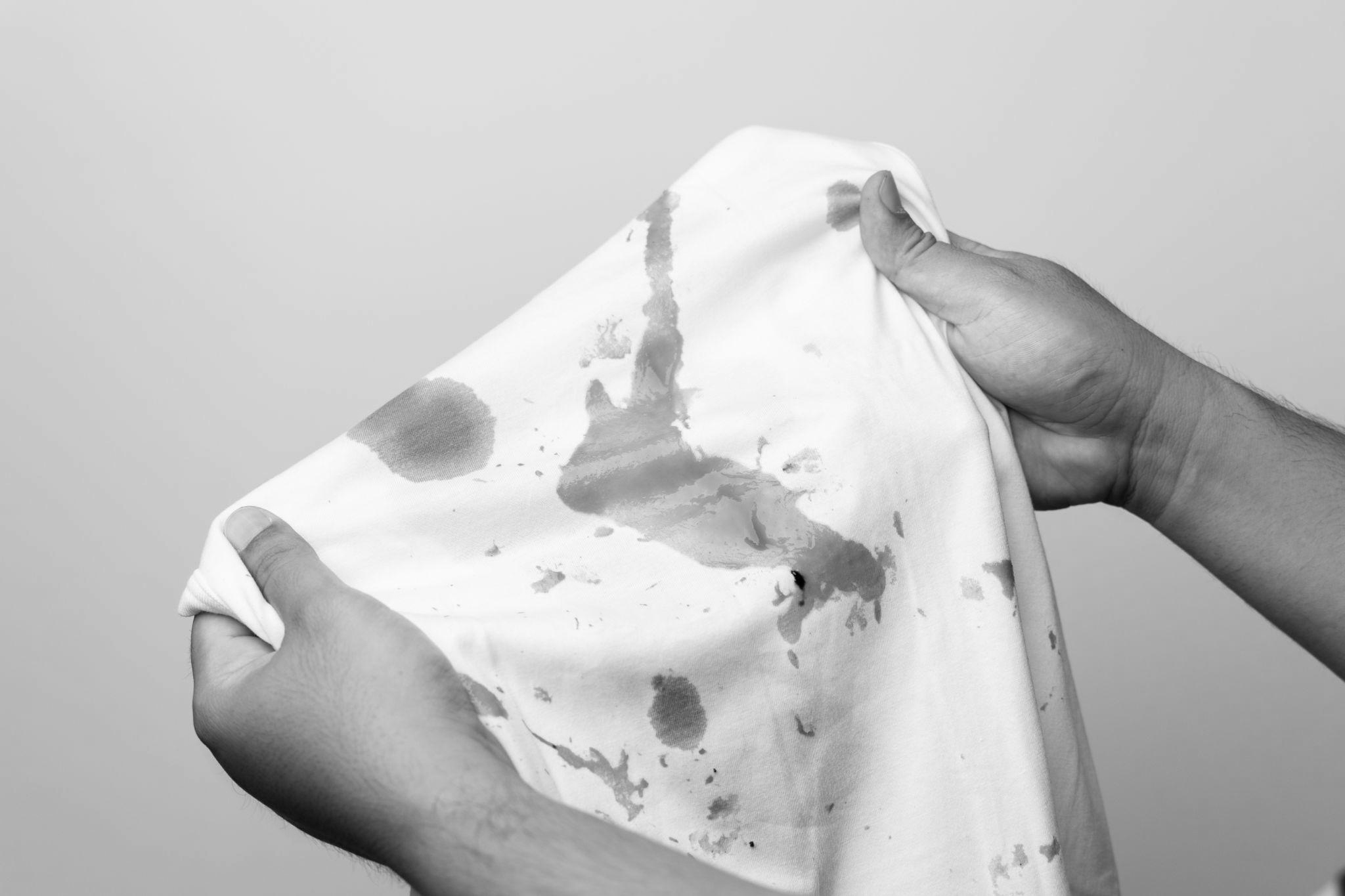 White shirt so many stains and dirt. Stained ketchup The man's hand held the shirt and opened it to look at the dirt.