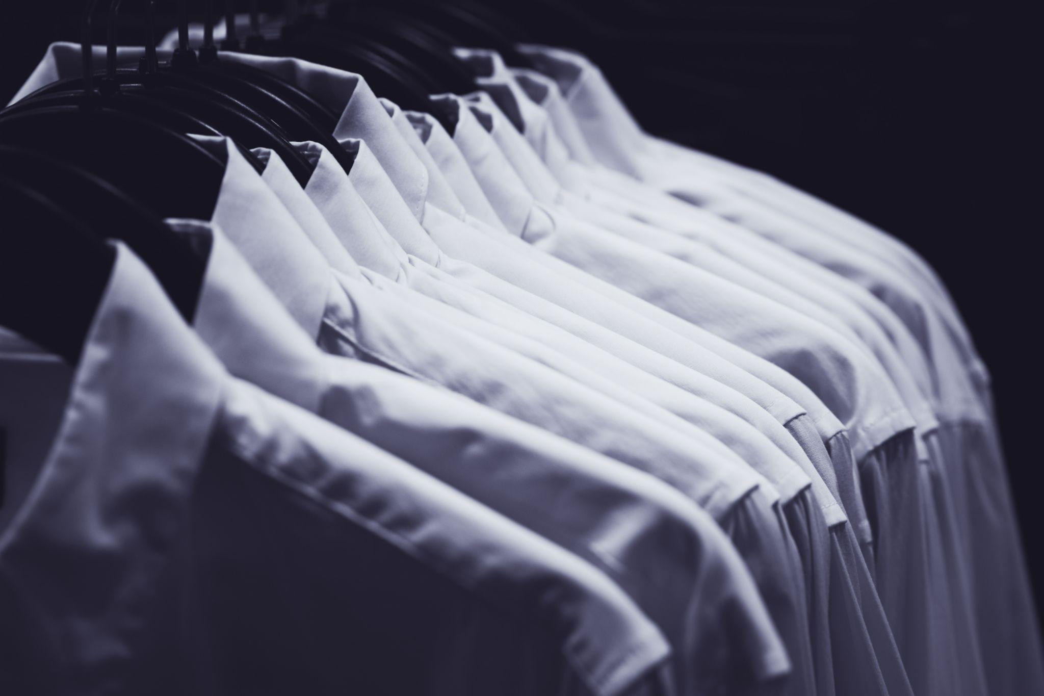 Row of white shirts hang on hangers in the darkness