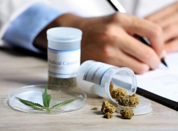 Doctor writing on prescription blank and bottle with medical cannabis on table close up