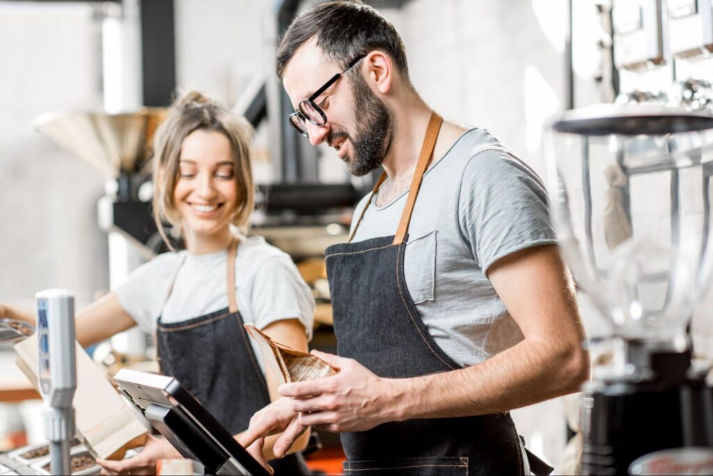 A Man and Woman Wearing a Black Barista Apron Uniform While Working at a Coffee Shop