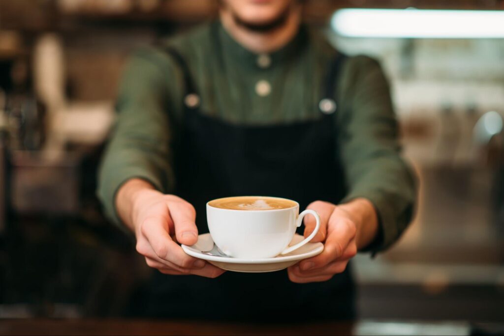 Coffee Shop Employee Wearing a Black Apron and Serving a Coffee