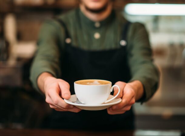 Coffee Shop Employee Wearing a Black Apron and Serving a Coffee